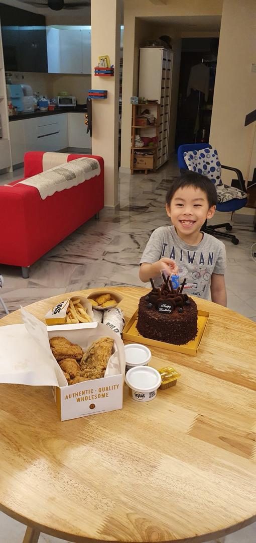 Wei Heng grinning beside a chocolate cake and fried chicken