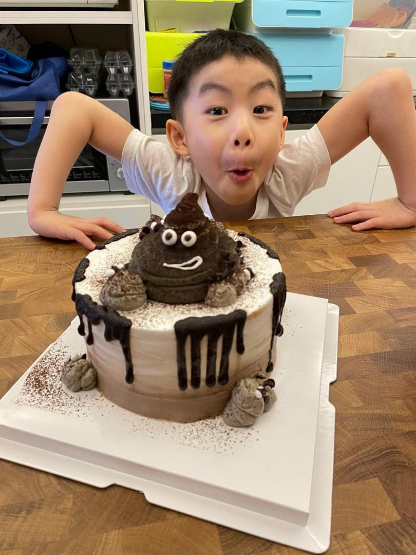 Wei Heng making a surprised face behind a poop-emoji cake