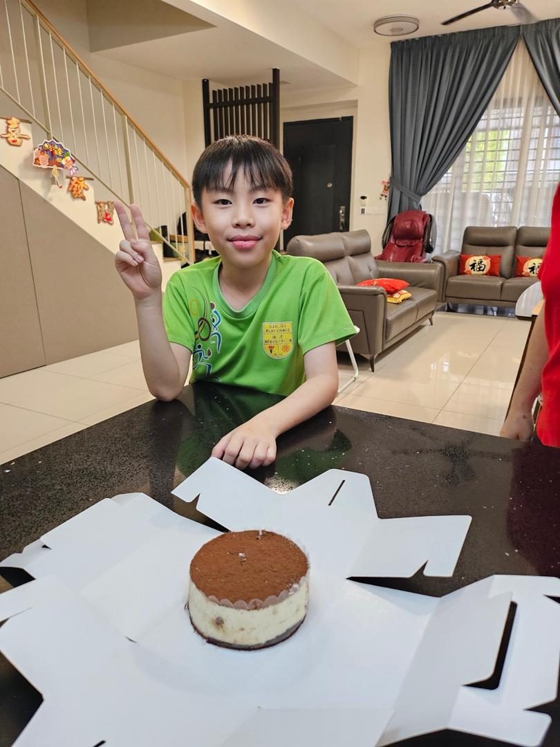 Wei Heng making a peace sign beside a tiramisu cake